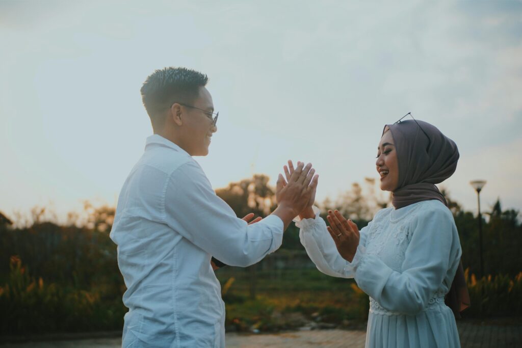Muslim couple in white outfits holding hands outdoors at sunset