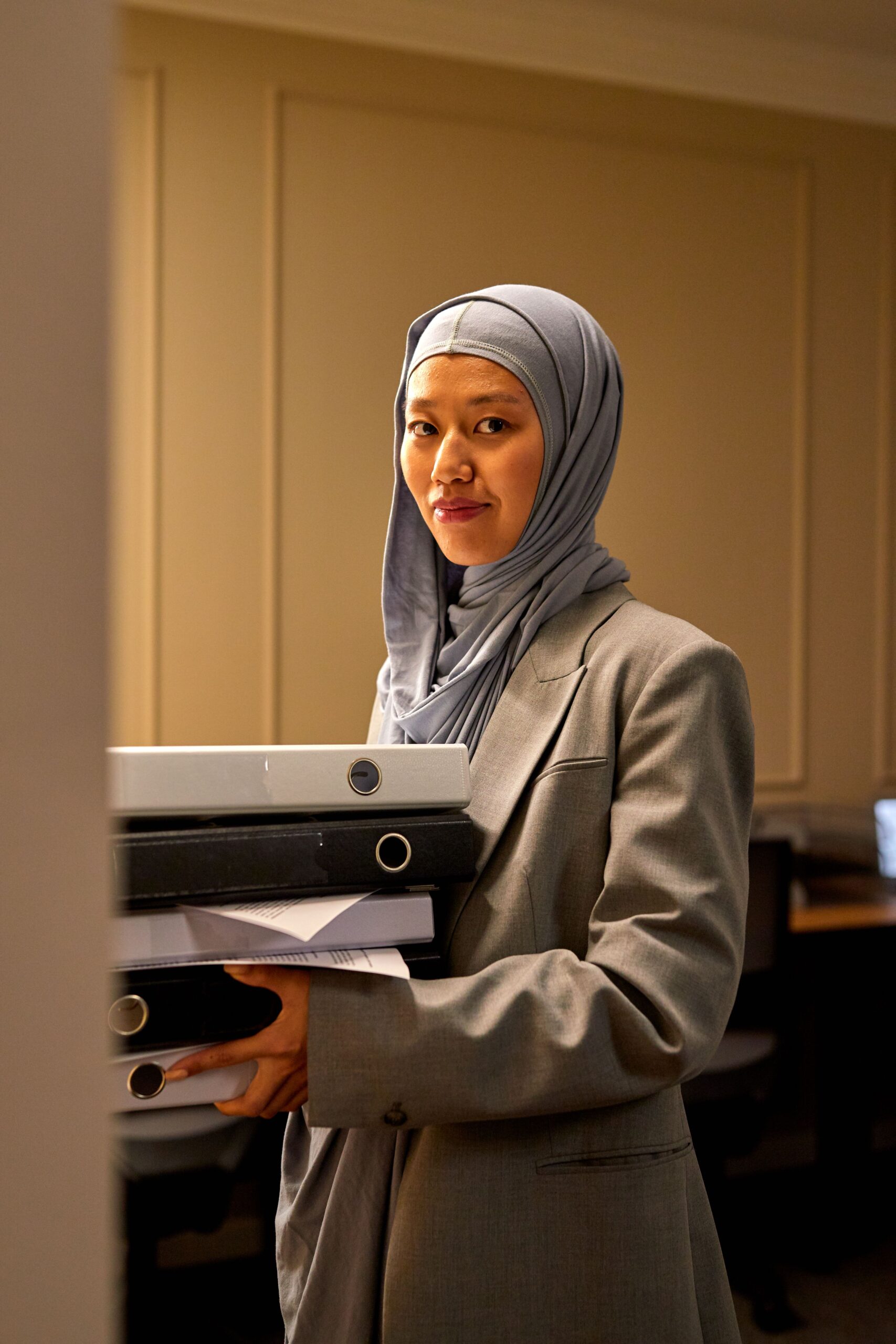 Femme d'affaires confiante en hijab et tailleur gris portant des dossiers au bureau