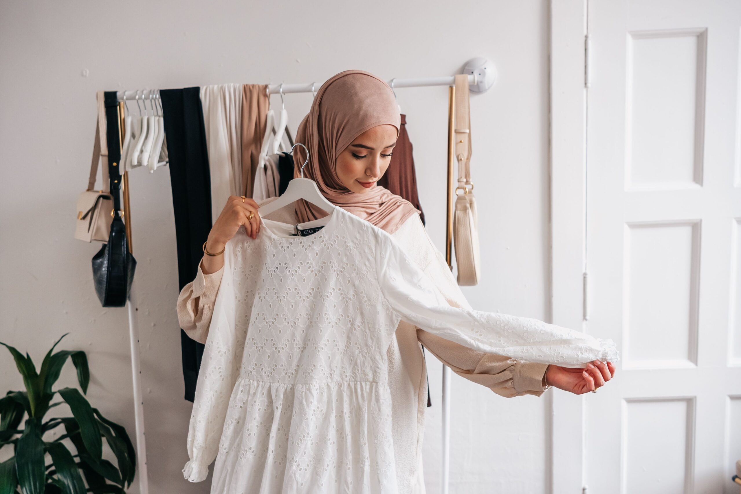 Femme en hijab examinant une robe blanche dans une boutique de vêtements