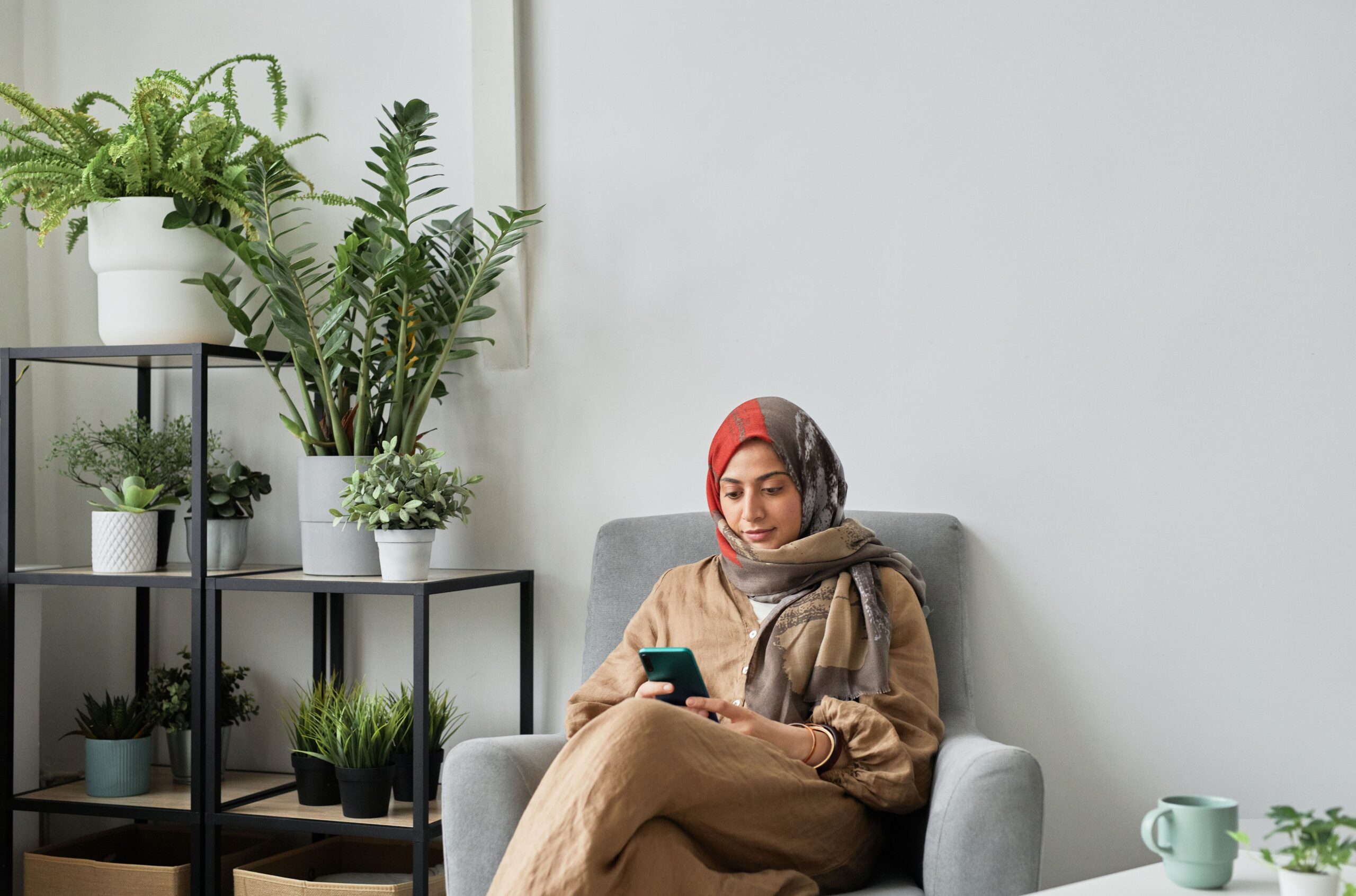 Femme en hijab se relaxant confortablement dans un fauteuil à la maison avec des plantes
