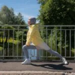 Femme en tenue de sport et hijab réalisant des étirements sur un pont avec un paysage verdoyant en arrière-plan
