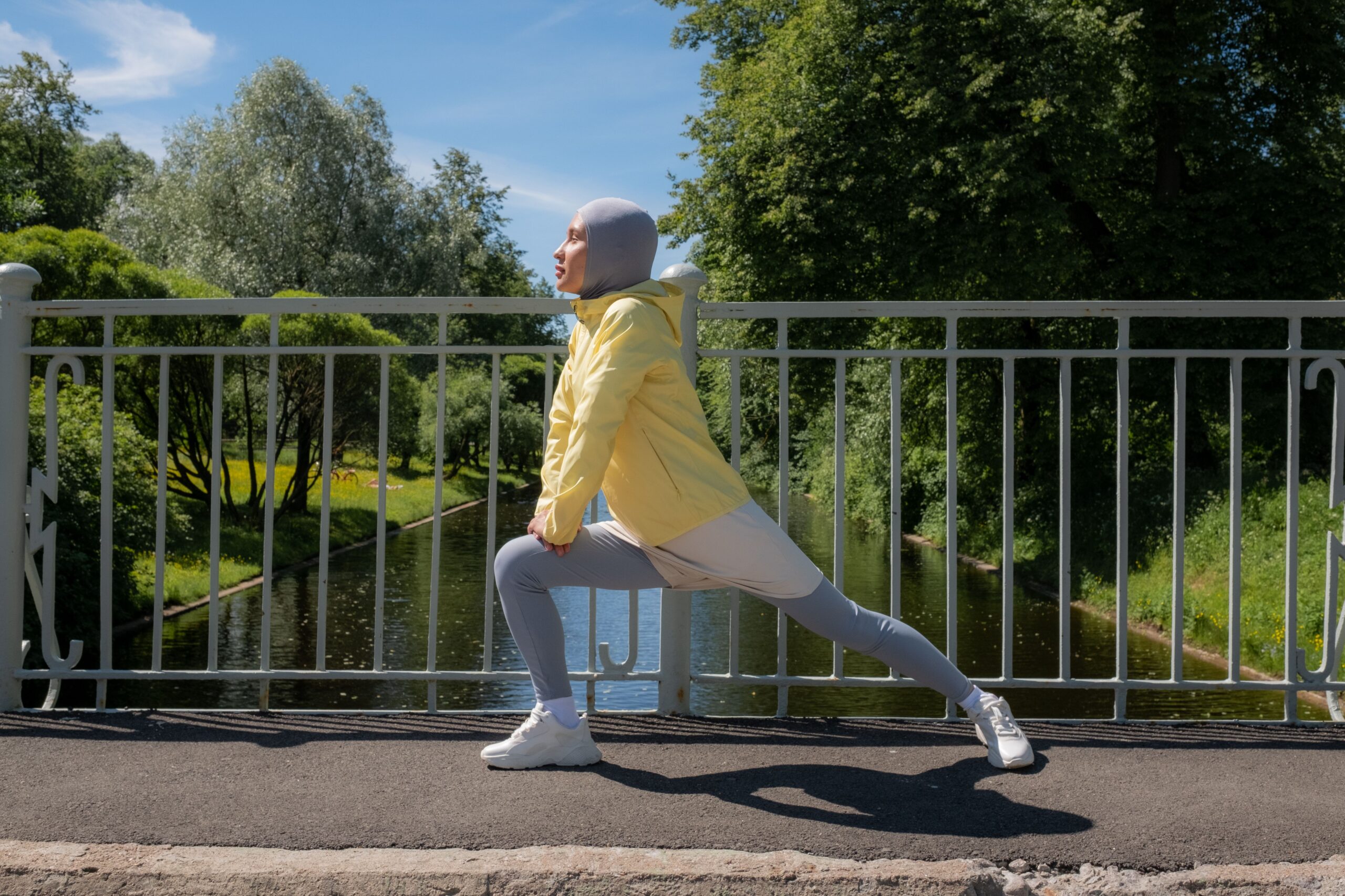 Femme en tenue de sport et hijab réalisant des étirements sur un pont avec un paysage verdoyant en arrière-plan