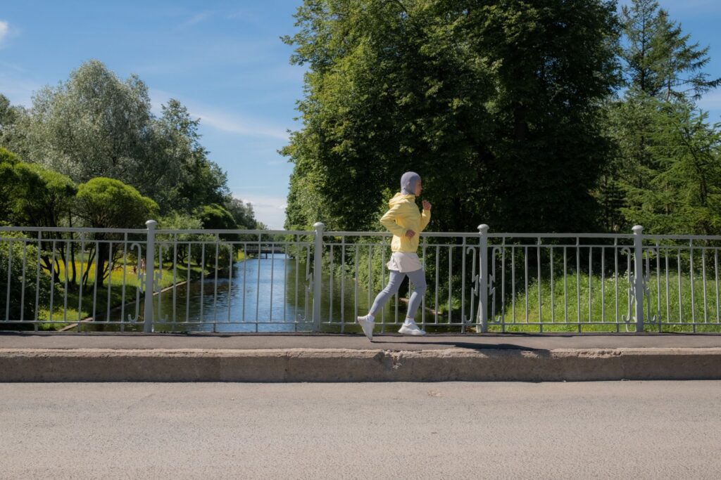 Femme voilée en tenue de sport jaune courant le long d'un canal dans un parc verdoyant