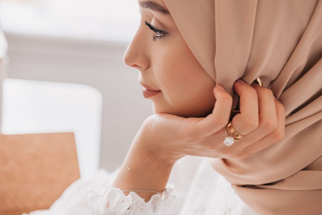 Gros plan sur une femme portant un hijab beige avec des bagues dorées délicates et un collier fin