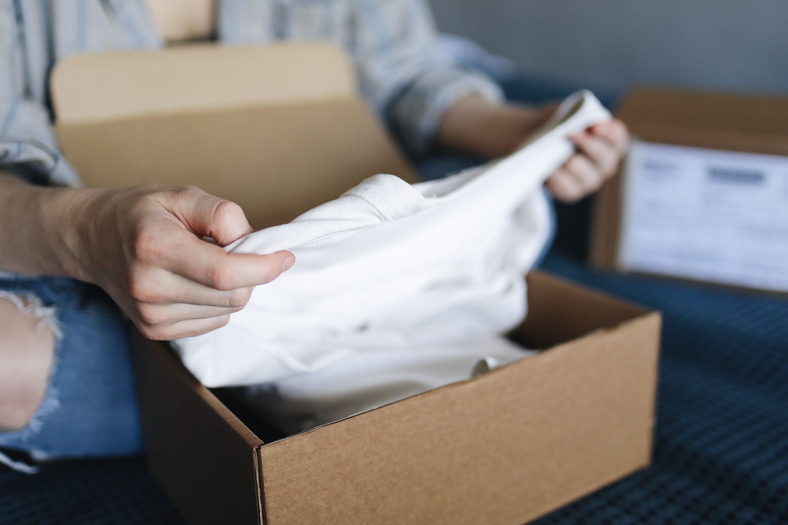 Personne déballant un vêtement blanc reçu dans un colis en carton