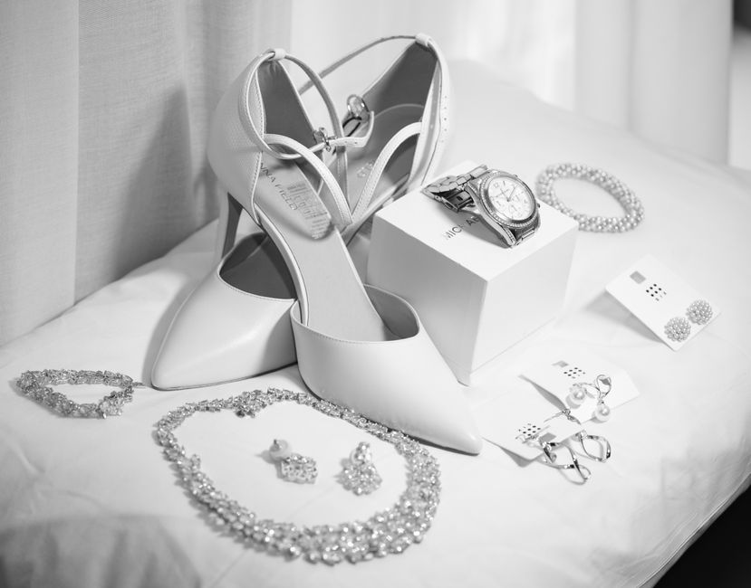 Elegant wedding accessories arranged on a light background: white high-heeled shoes and refined jewelry
