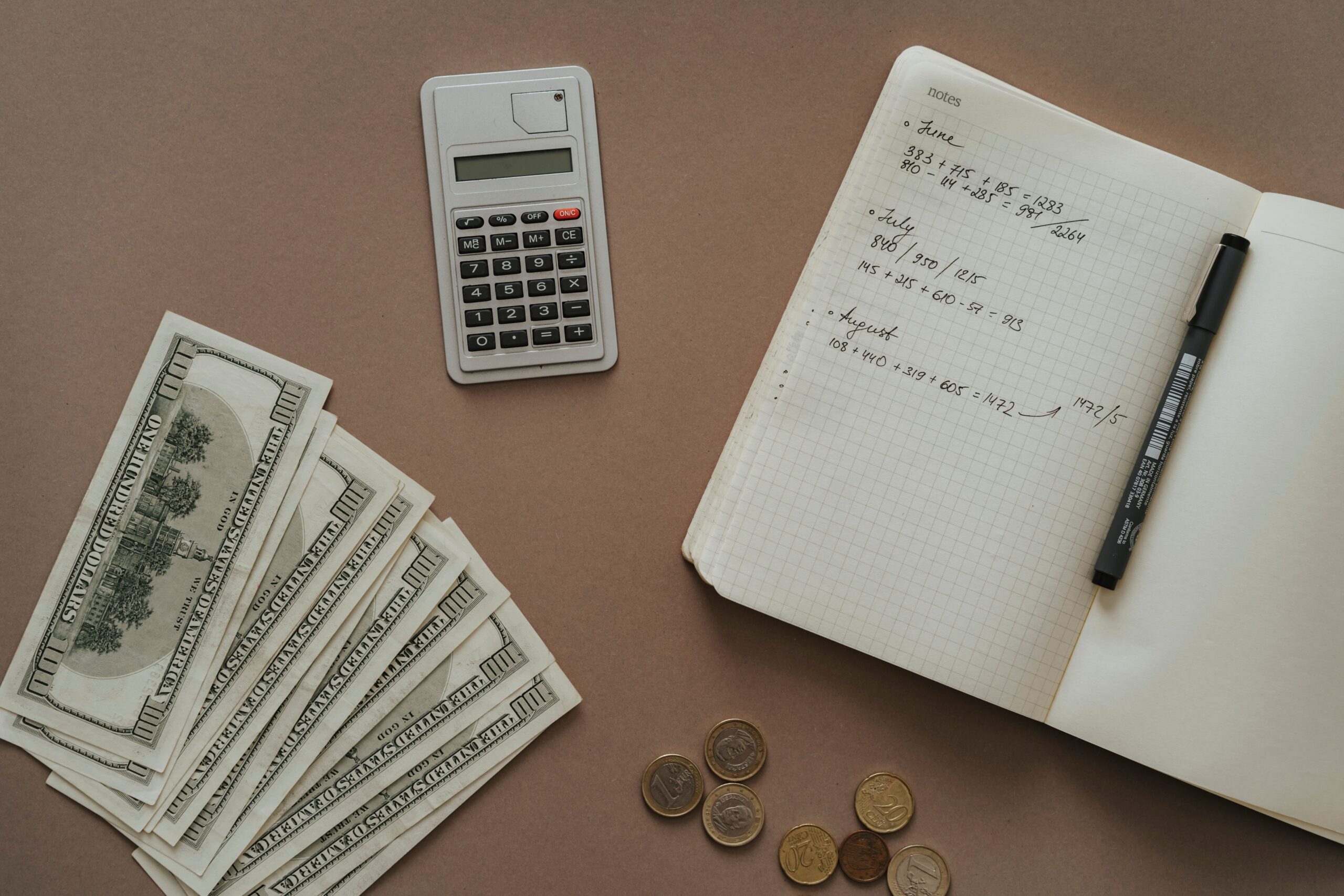 Calculatrice, carnet avec notes financières et billets en dollars sur une table, symbolisant la planification budgétaire d'un voyage