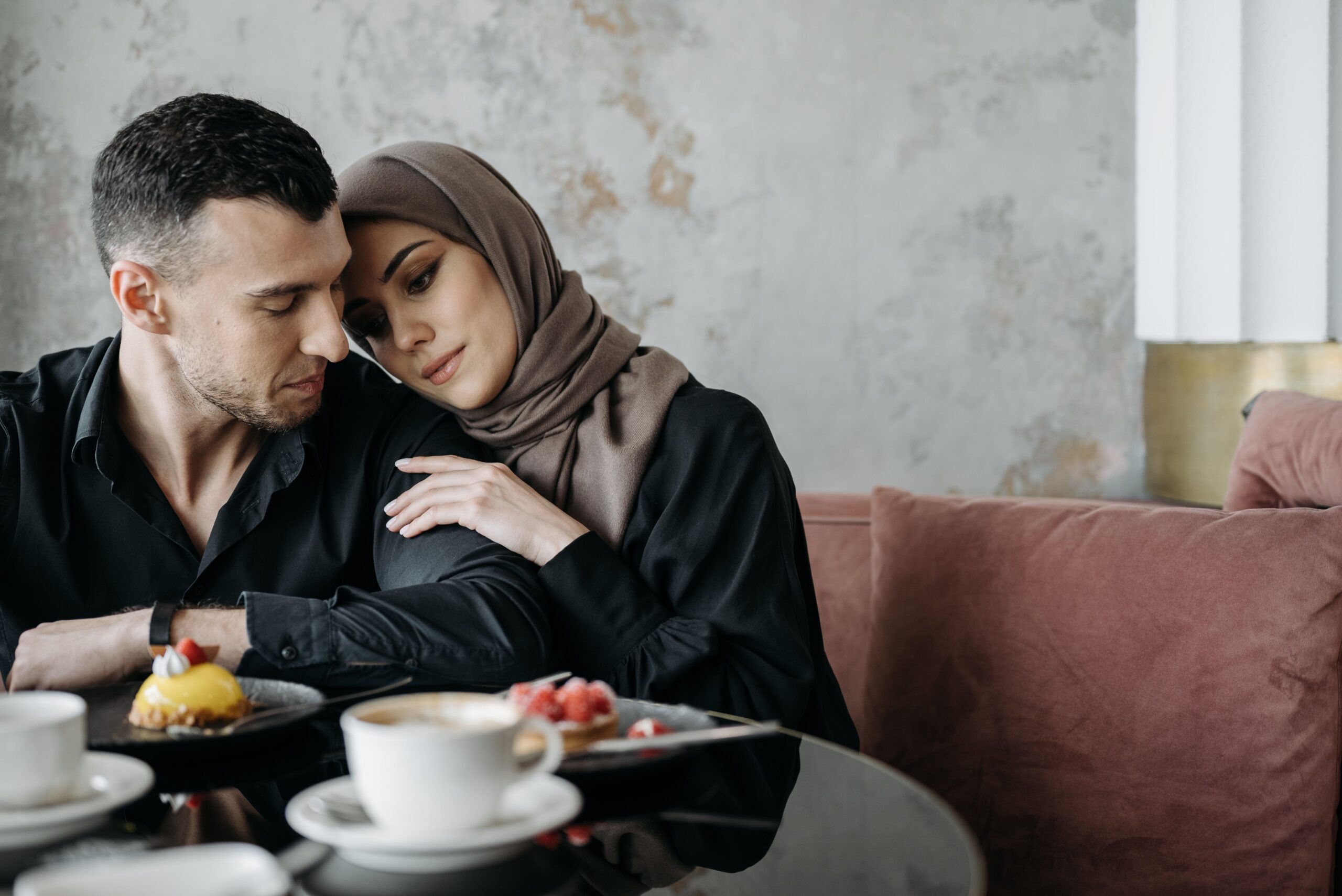Muslim couple sharing a tender, close moment in a café, wearing a hijab and modest clothing