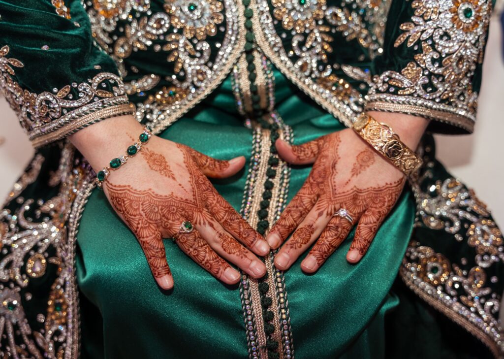 Détail des broderies luxueuses et perles sur un caftan vert avec mains ornées de henné