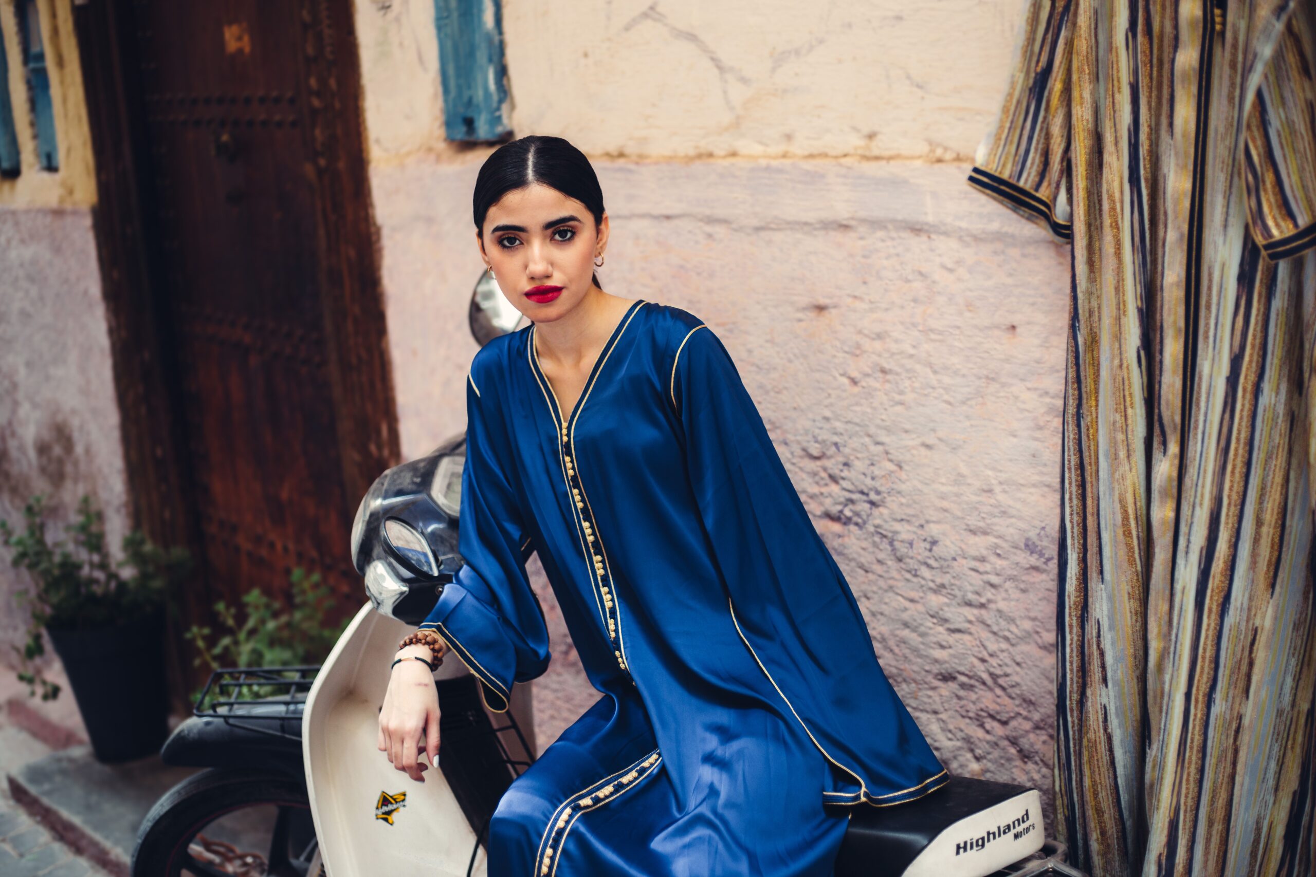 Femme en caftan bleu moderne assis sur un scooter dans un décor urbain