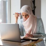 Femme portant le hijab étudiant avec un ordinateur portable et un livre ouvert