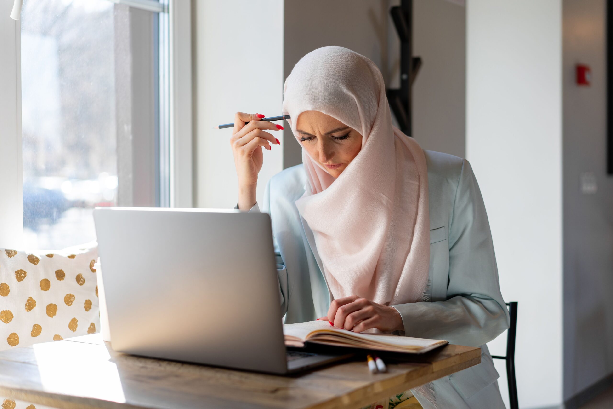 Femme portant le hijab étudiant avec un ordinateur portable et un livre ouvert