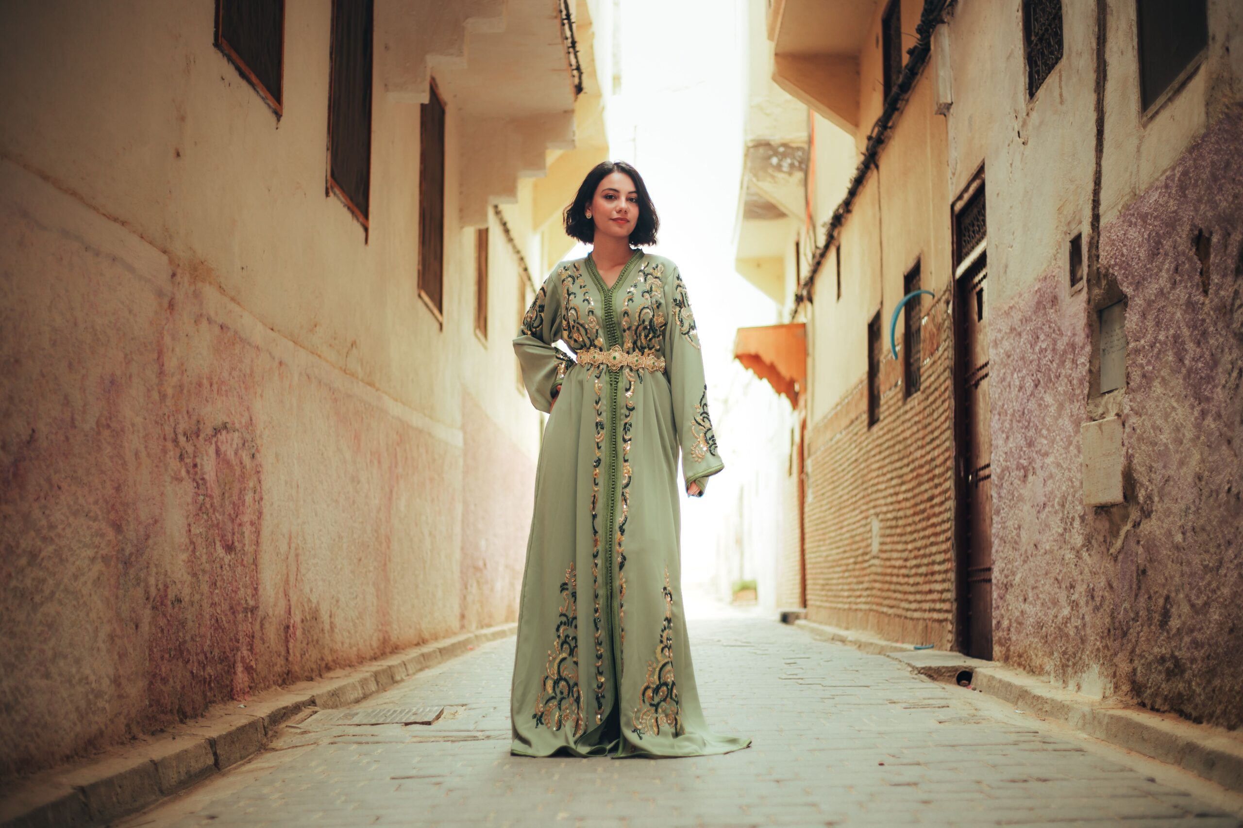 Femme portant un caftan marocain vert brodé dans une ruelle traditionnelle