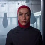 Femme portant un hijab rouge dans une salle de boxe avec des sacs de frappe