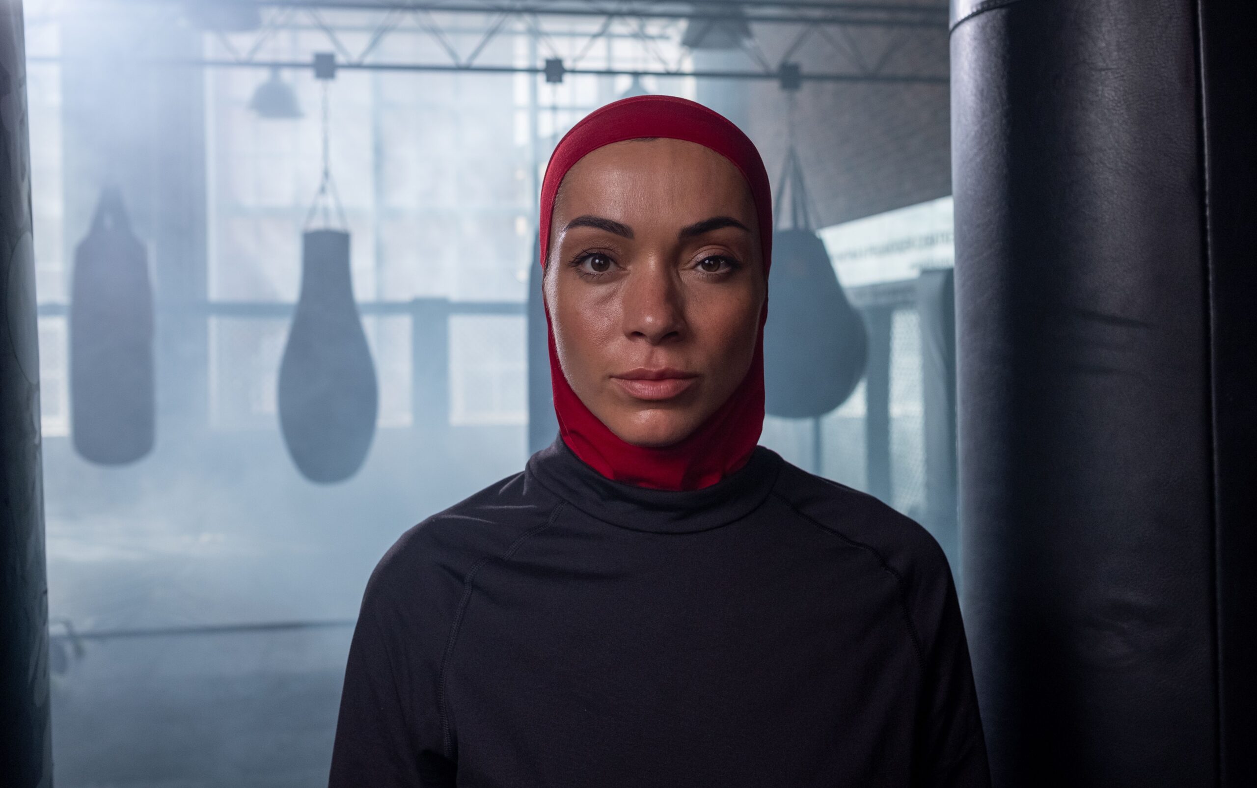 Femme portant un hijab rouge dans une salle de boxe avec des sacs de frappe