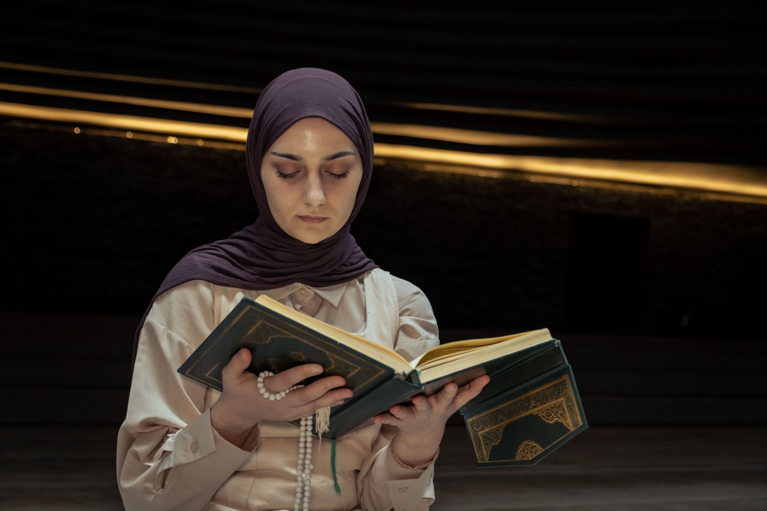 Femme portant un hijab tenant un livre de prière et priant dans une lumière douce