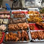 Grand buffet de street food avec brochettes de viandes grillées variées, légumes et plats chauds exposés