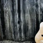 Guitare acoustique en bois posée contre un mur rustique