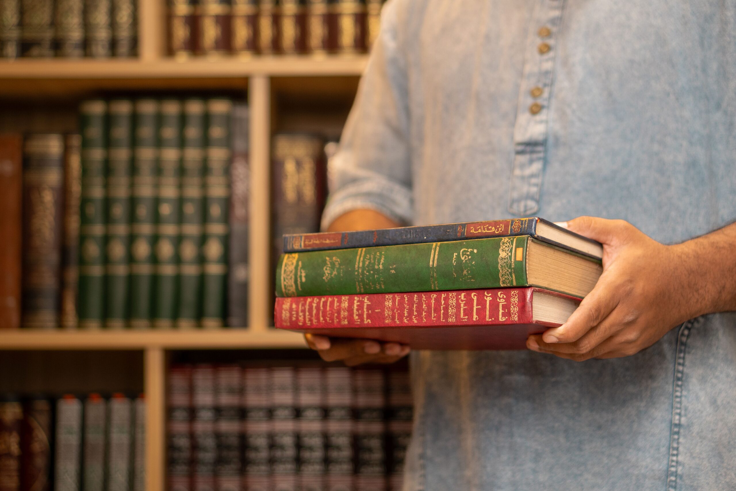 Homme dans une bibliothèque tenant une pile de livres islamiques en arabe