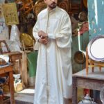 Homme en tenue traditionnelle blanche brodée dans un marché oriental montrant les chevilles découvertes