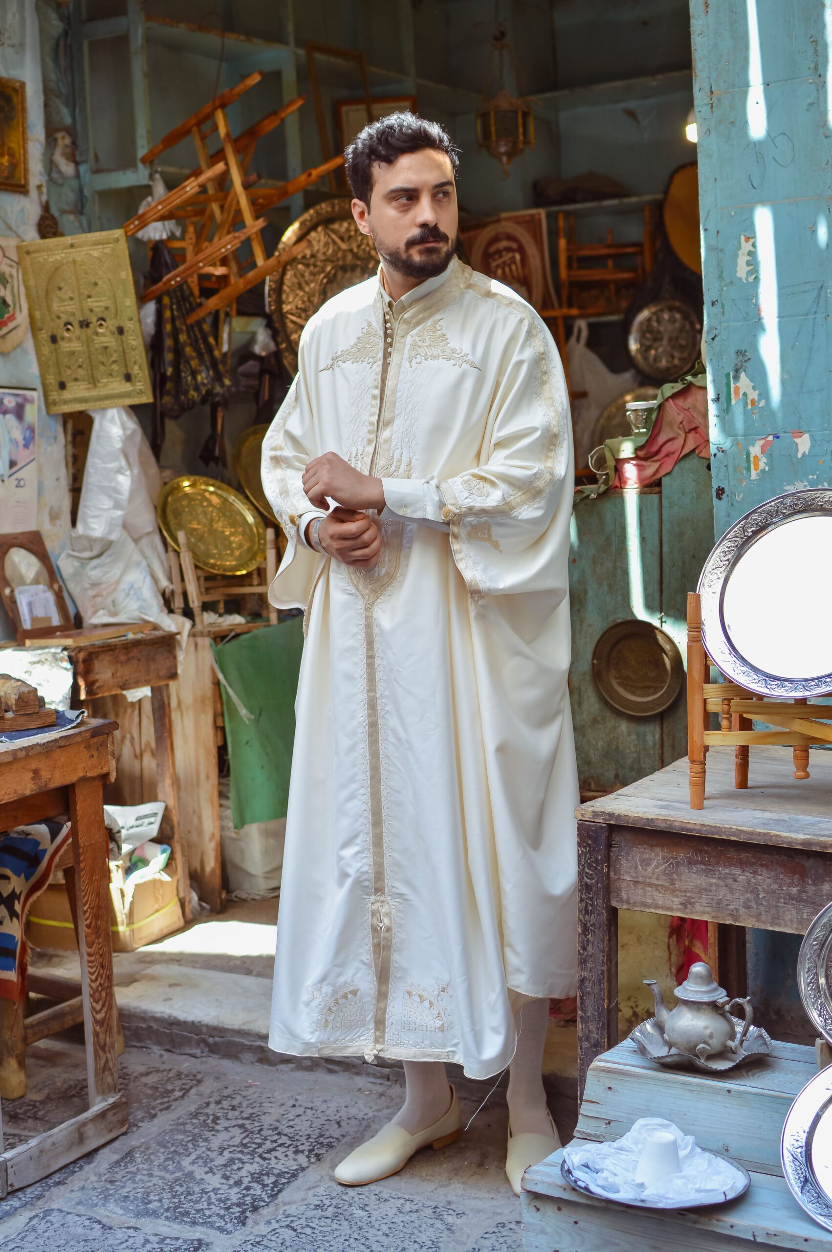 Homme en tenue traditionnelle blanche brodée dans un marché oriental montrant les chevilles découvertes