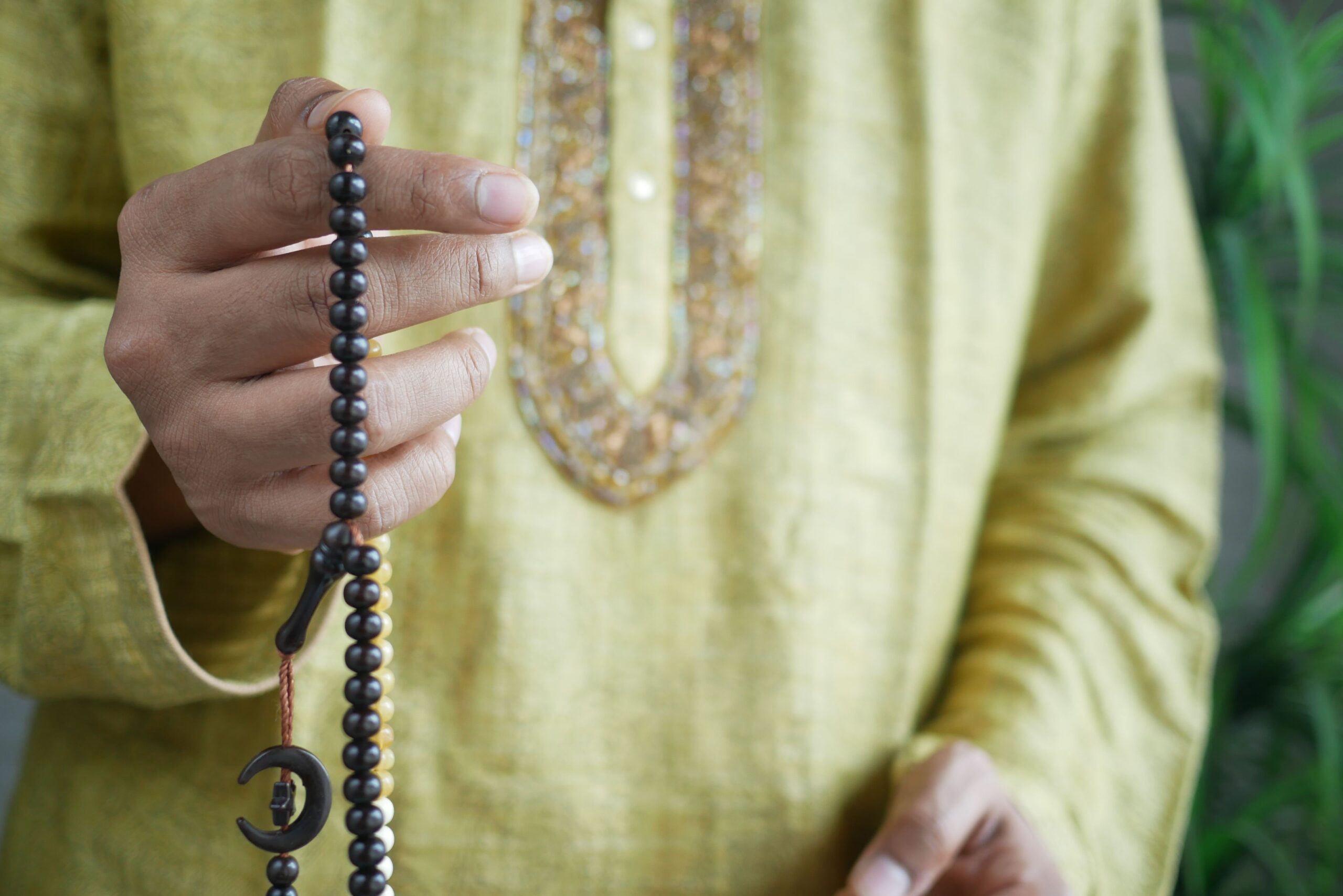Hand holding Muslim prayer beads with black beads for reciting dhikr