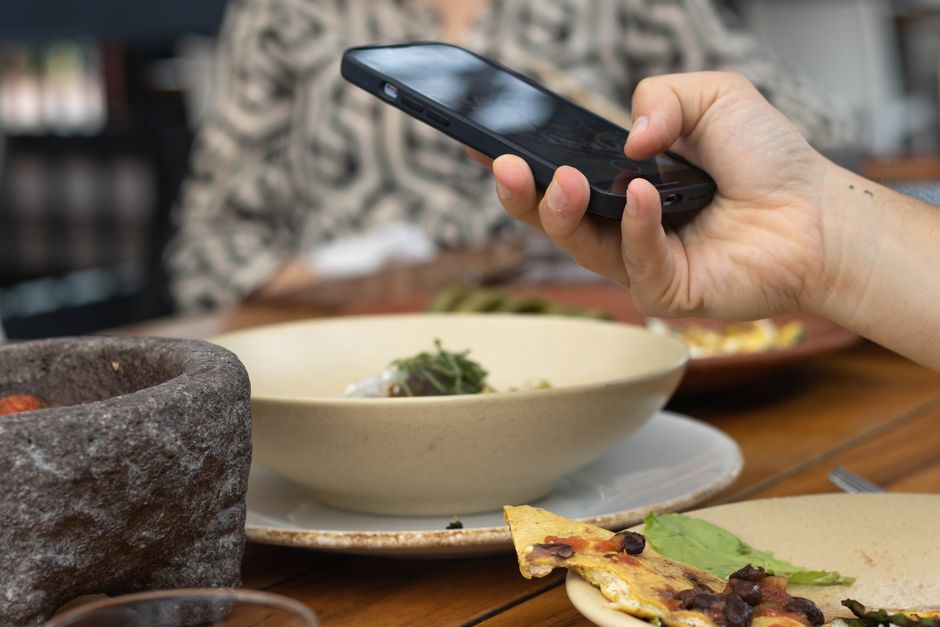 Main tenant un smartphone pour consulter des avis ou prendre une photo d'un plat au restaurant