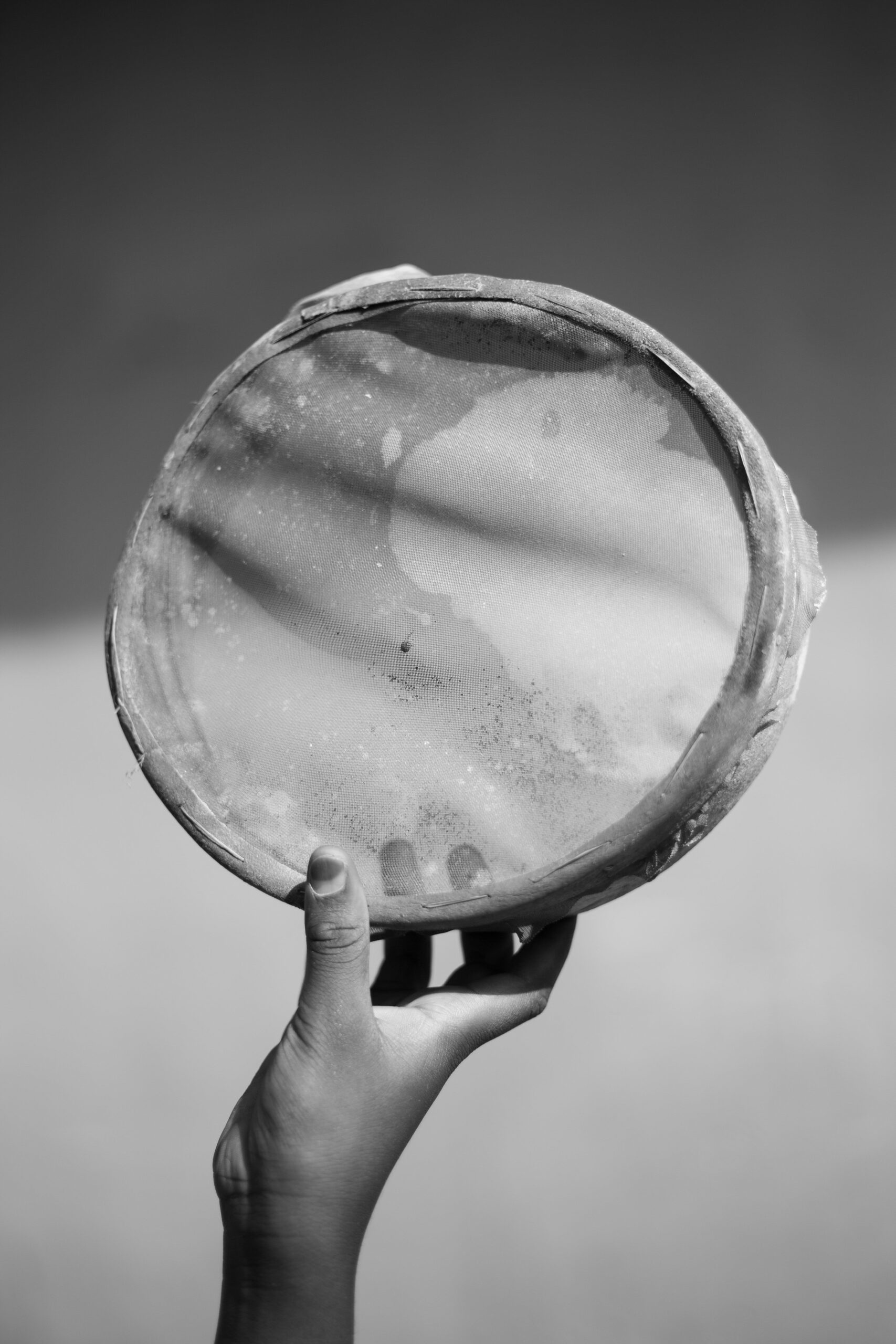 Hand holding a traditional round drum against a neutral background