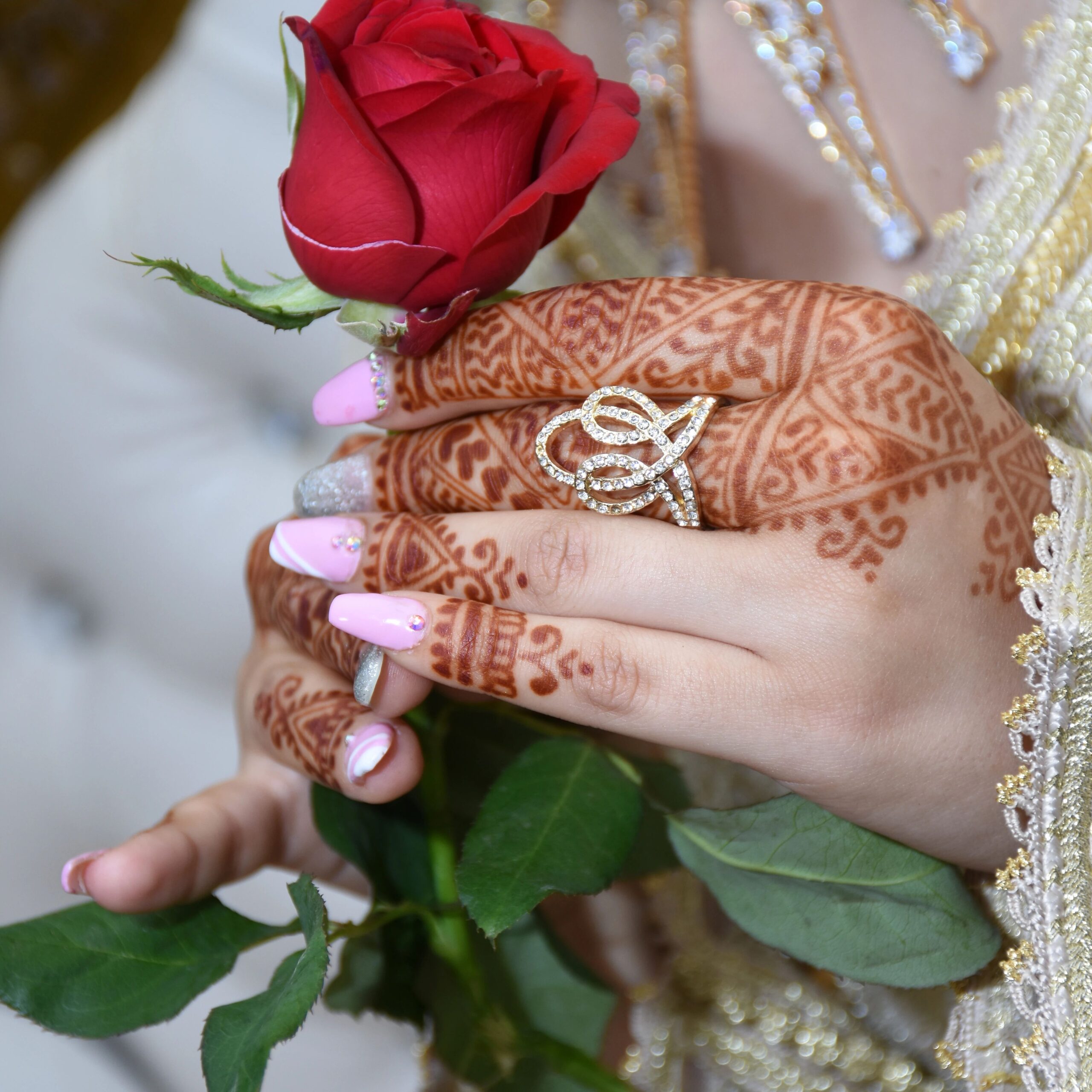 Mains de mariée ornées de henné traditionnel tenant une rose rouge