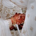 Mains de mariés musulmans ornées de henné se tenant lors de la cérémonie de mariage, avec tenues traditionnelles blanches brodées d'or