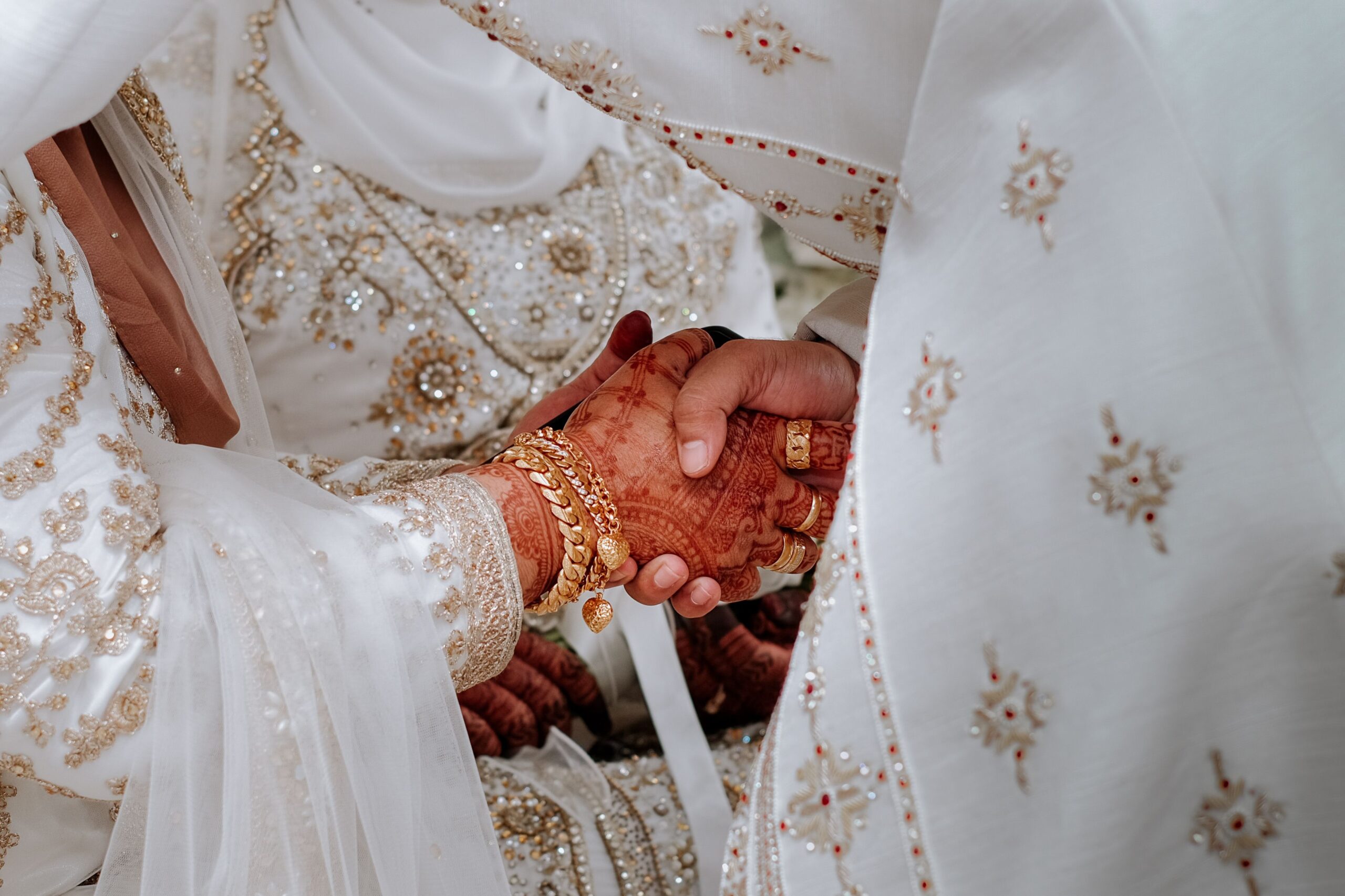 Mains de mariés musulmans ornées de henné se tenant lors de la cérémonie de mariage, avec tenues traditionnelles blanches brodées d'or