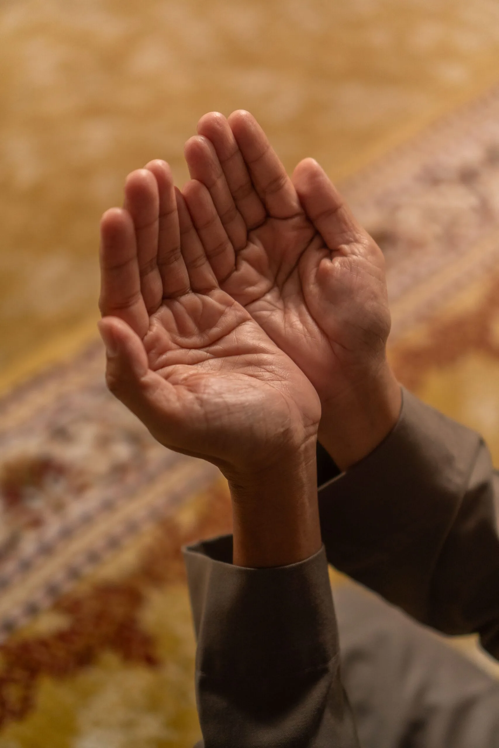 Mains levées en position de prière sur un tapis de prière orné
