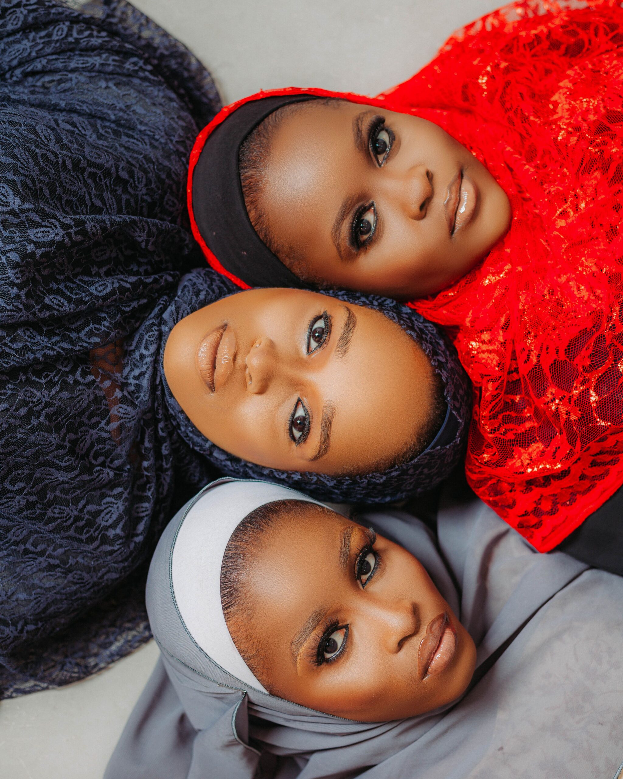 Portrait de trois femmes portant des hijabs dans des tons contrastés noir, rouge vif et gris, illustrant la diversité des styles modernes