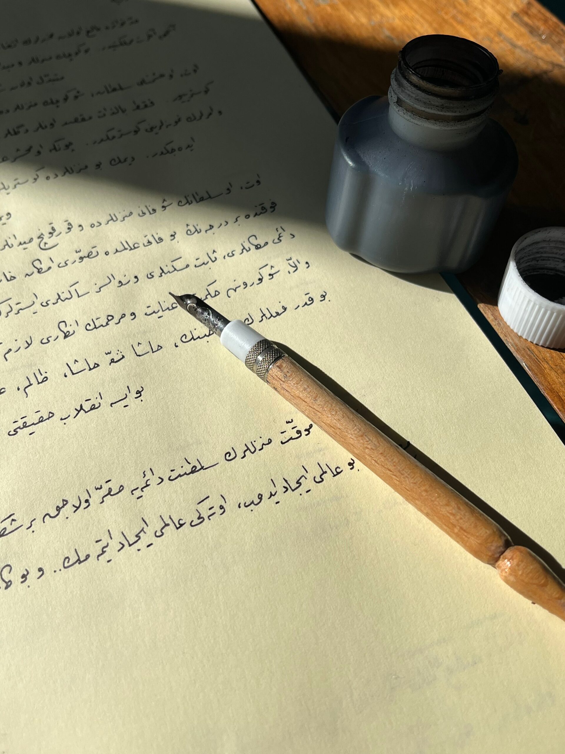 Stylo de calligraphie traditionnel posé sur du papier avec écriture arabe et flacon d'encre