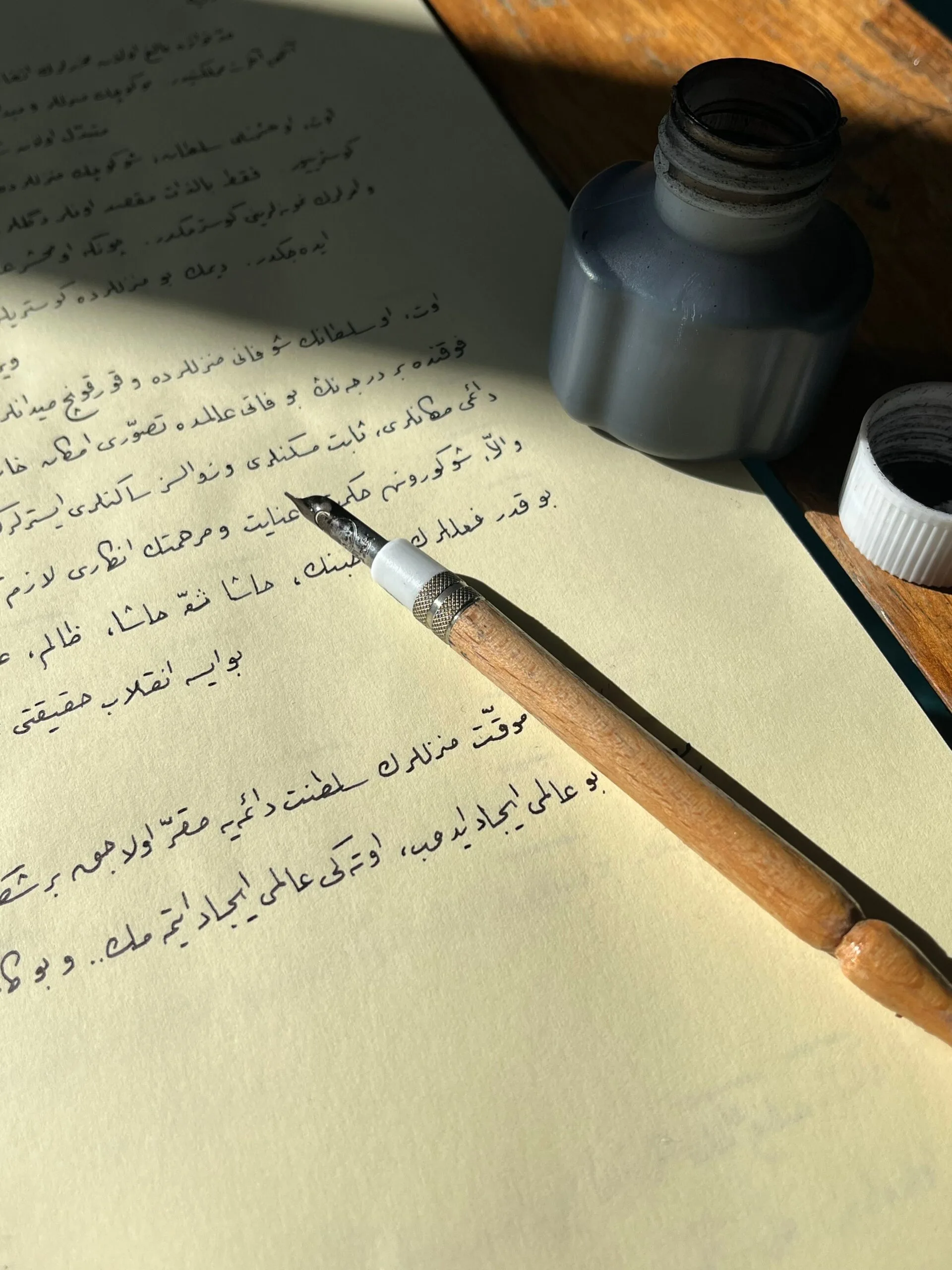 Stylo de calligraphie traditionnel posé sur du papier avec écriture arabe et flacon d'encre