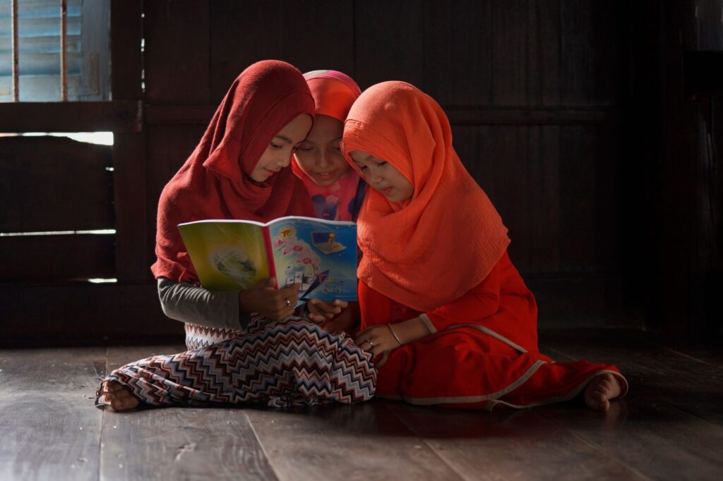 Trois jeunes filles portant le hijab lisant ensemble un livre illustré