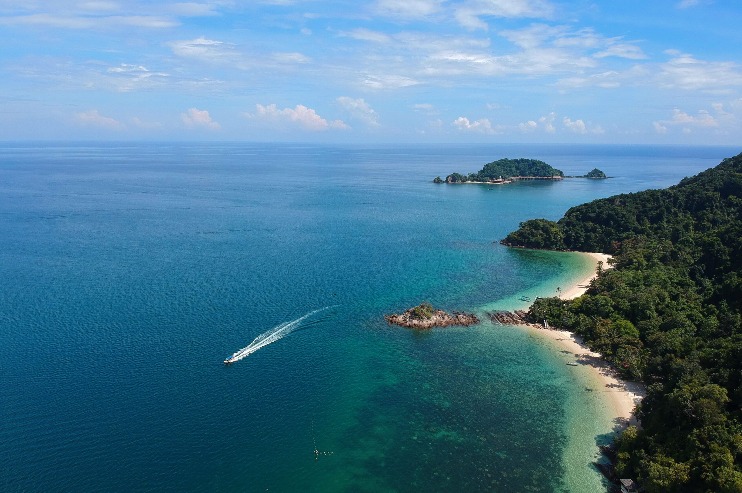 Vue aérienne d'une île tropicale malaisienne entourée d'eaux turquoise cristallines avec un bateau naviguant près de la côte